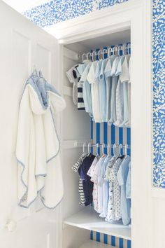 a closet with blue and white wallpaper and clothes hanging on the rack in it