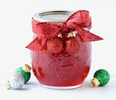 a glass jar filled with red liquid and christmas decorations next to it on a white surface