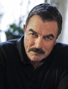 a man with a moustache on his face looking at the camera while wearing a black shirt