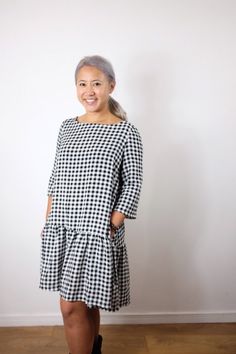 a woman standing in front of a white wall wearing a black and white checkered dress