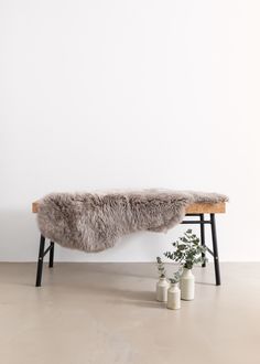 a bench with a fur cover on it next to some vases and a plant