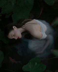 a woman laying down in the water surrounded by leaves