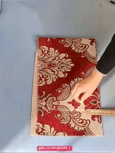 a person is cutting up a red and white rug with a ruler on the floor