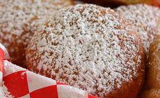 powdered sugar covered donuts sitting on top of red and white checkered napkins