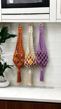 three macrame bags hanging on the wall in front of a microwave and potted plant