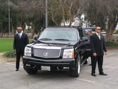 two men in suits standing next to a black limo