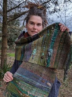 a woman holding up a multicolored shawl in the woods