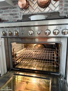 an oven with two copper pots on the wall above it and one is open to show food cooking inside