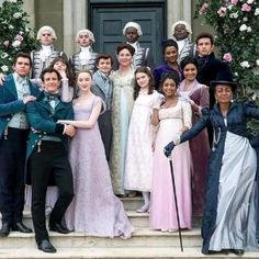 a group of people standing on steps in front of a building with flowers and bushes