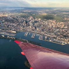 an airplane wing flying over a large body of water with buildings and bridges in the background