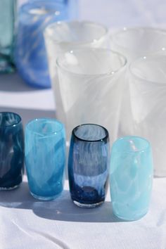 several different colored glasses sitting on top of a white table covered in blue and white cloth