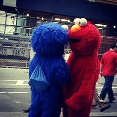 two people dressed as sesame and elm street characters standing on the sidewalk in front of a building