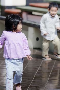 two young children are playing in the rain on a tile floor, one is holding an umbrella