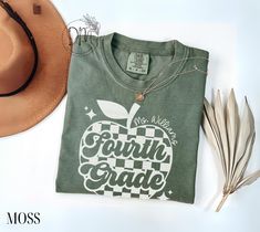 an apple t - shirt with the words fourth grade on it next to a hat