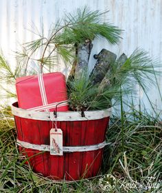 a red bucket filled with christmas presents sitting on top of a grass covered field next to a white wall