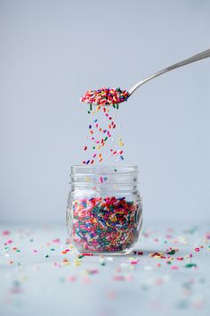 sprinkles are being poured into a jar with a spoon on the table