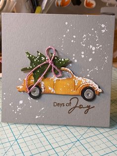 a yellow car with a christmas tree on the roof is sitting in front of a card that says, days of joy