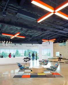 people are standing in an open space with chairs and lights hanging from the ceiling above