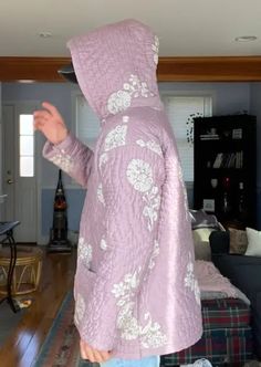 a person in a purple jacket is standing in a living room and looking at something