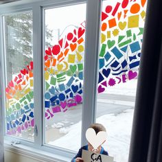 a child holding up a paper cutout in front of a window