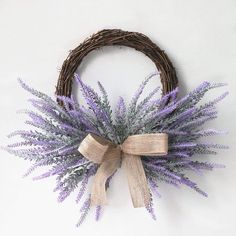 a wicker wreath with purple flowers and a bow hanging on the front of it