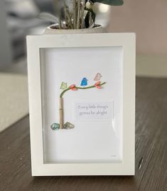 a small white frame with flowers in it sitting on a table next to a potted plant