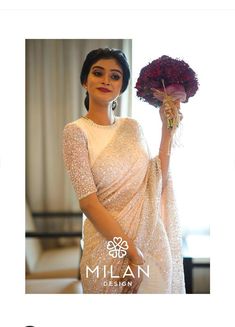 a woman holding a bouquet of flowers in her hand and wearing a white sari