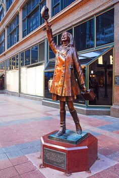 a statue of a woman with a hat and purse in front of a large building