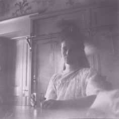 an old black and white photo of a woman sitting at a table with a glass in her hand