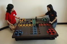 two people playing a board game in a room with white walls and black flooring