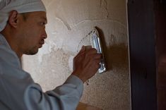 a man in a white robe painting a wall with paint rollers and a brush