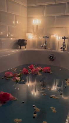 rose petals floating on the surface of a bathtub with candles in the back ground