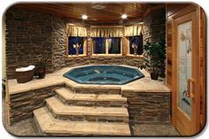 an indoor hot tub with steps leading up to it and a stone wall behind it