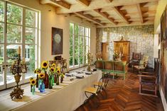 a long table with sunflowers and vases on it in front of large windows