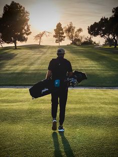 a man walking across a lush green field holding two skateboard's in his hands