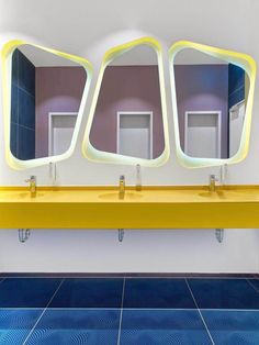 three yellow sinks with mirrors above them on the wall and blue flooring in front of them