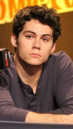 a young man sitting at a table with a cell phone in his hand and looking off to the side