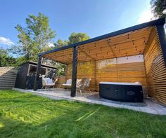 a hot tub sitting under a pergolated roof next to a wooden structure on top of a lush green field