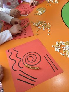 two children are sitting at a table making crafts with paper and gold beads on it