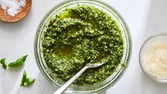 a glass bowl filled with pesto next to two bowls of cheese and seasoning