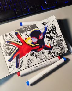 a spiderman themed notebook with markers on the side and a keyboard in the background