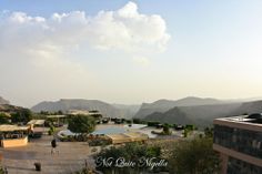 a person is standing on the roof of a building overlooking a pool and mountains in the distance