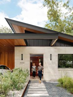 two women walking into a modern home with wood and stone accents on the front door