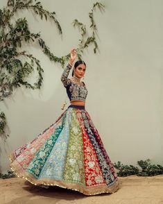 a woman in a multicolored lehenga dancing with her arms raised up