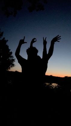 a person with their arms up in the air at sunset or dawn, silhouetted against a dark sky