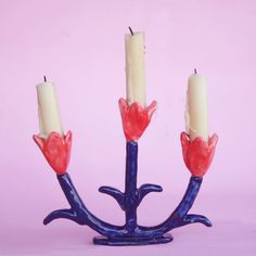 three candles with red and white flowers are in a blue candle holder on a pink background