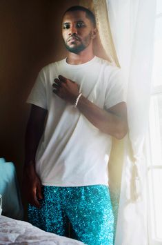 a man standing in front of a window wearing blue and green sequins on his pants