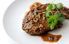 a white plate topped with meat covered in sauce and garnished with cilantro