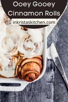 cinnamon rolls with icing in a white dish on a table next to a book