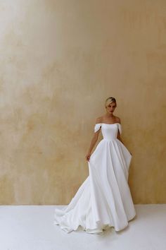 a woman in a white wedding dress standing against a wall with her hands on her hips